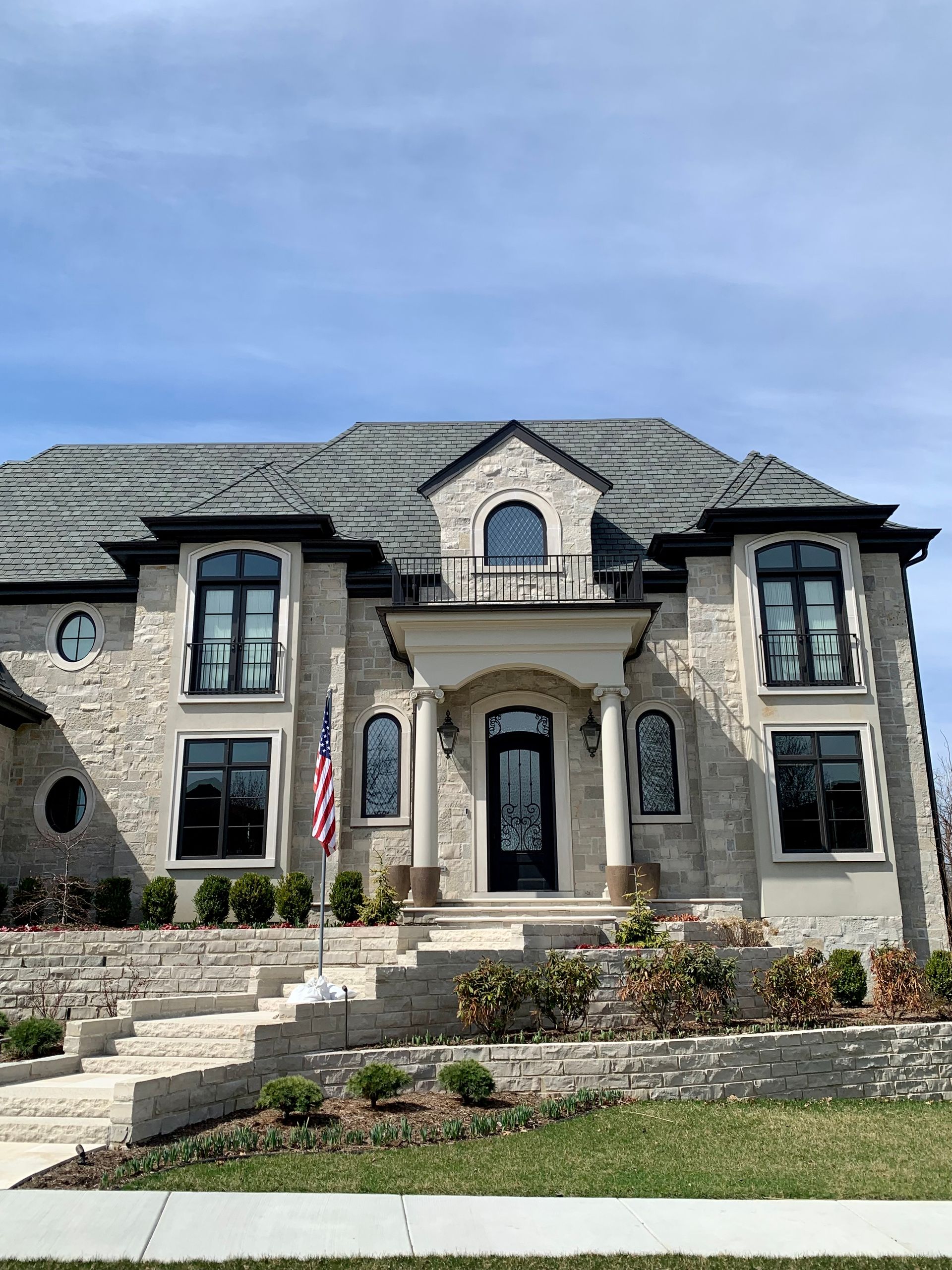 Stone mansion with black-framed windows, black door, US flag, blue sky.