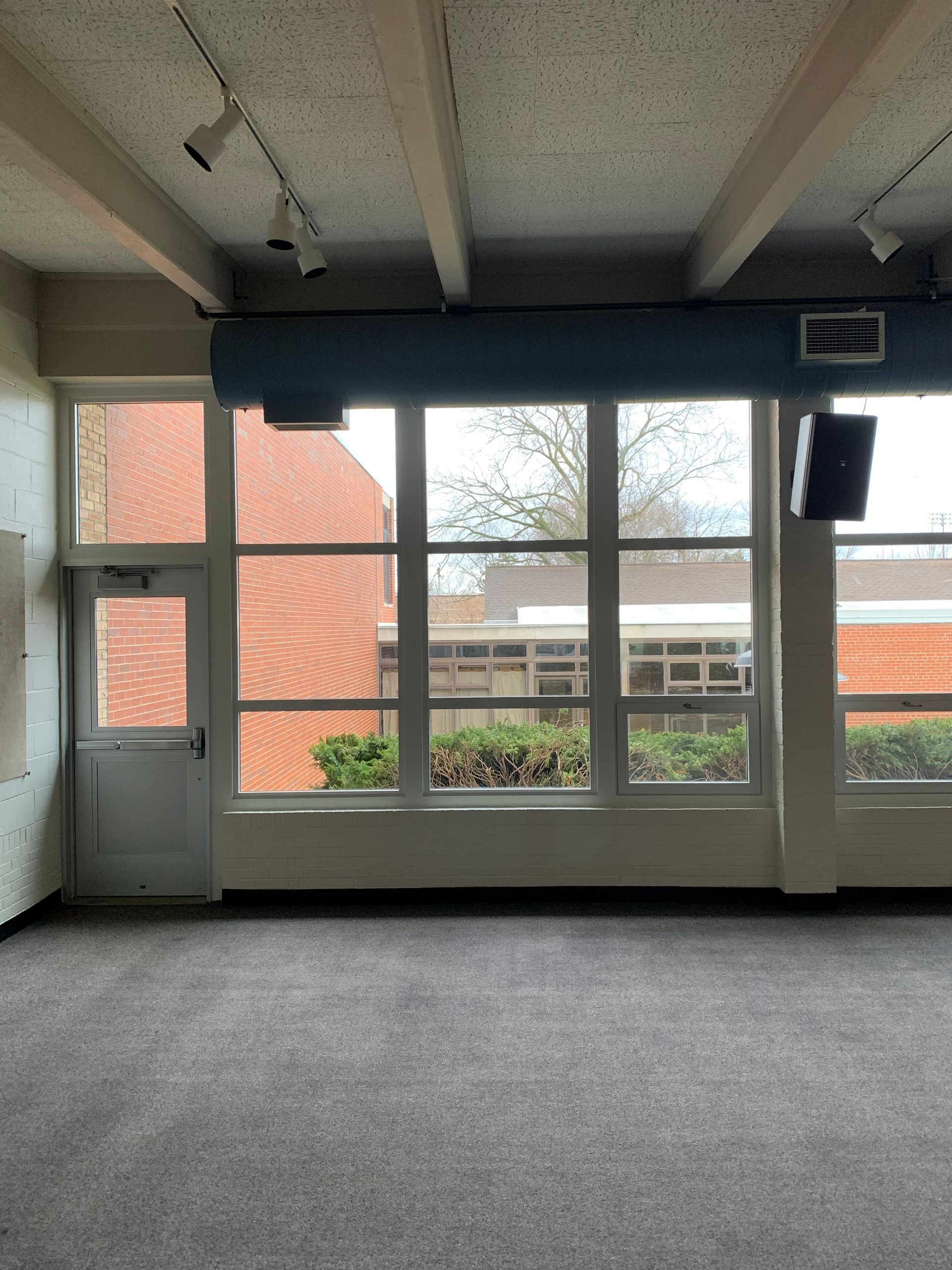 Empty room with door, large windows, brick exterior visible, gray carpet.