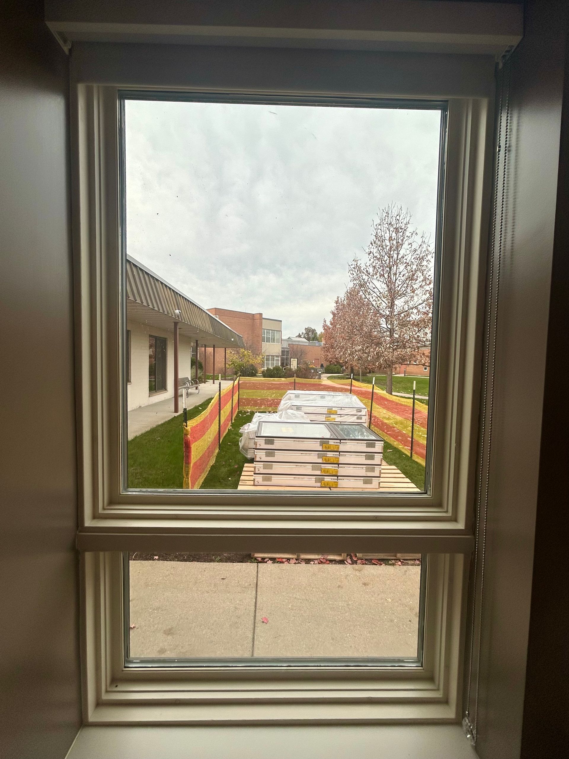 View through a window of construction materials and a building beyond a barrier on a cloudy day.
