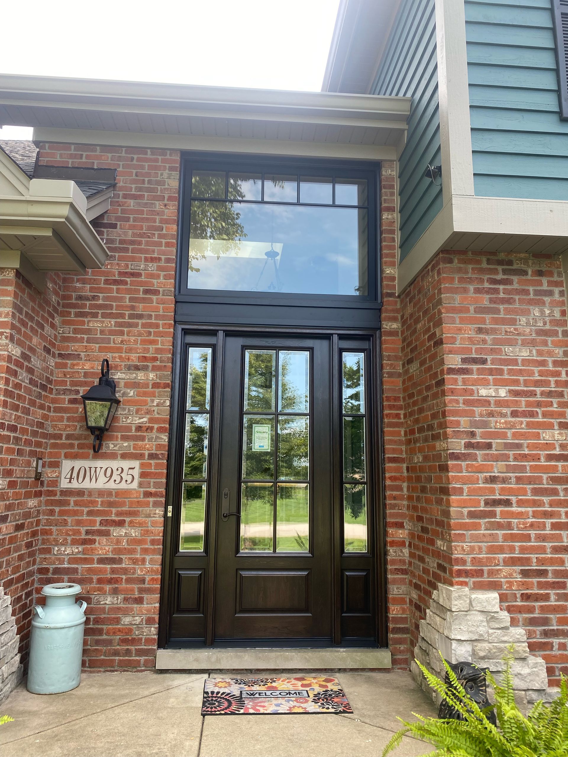 Red brick home entrance with dark brown door, large window, and colorful welcome mat.