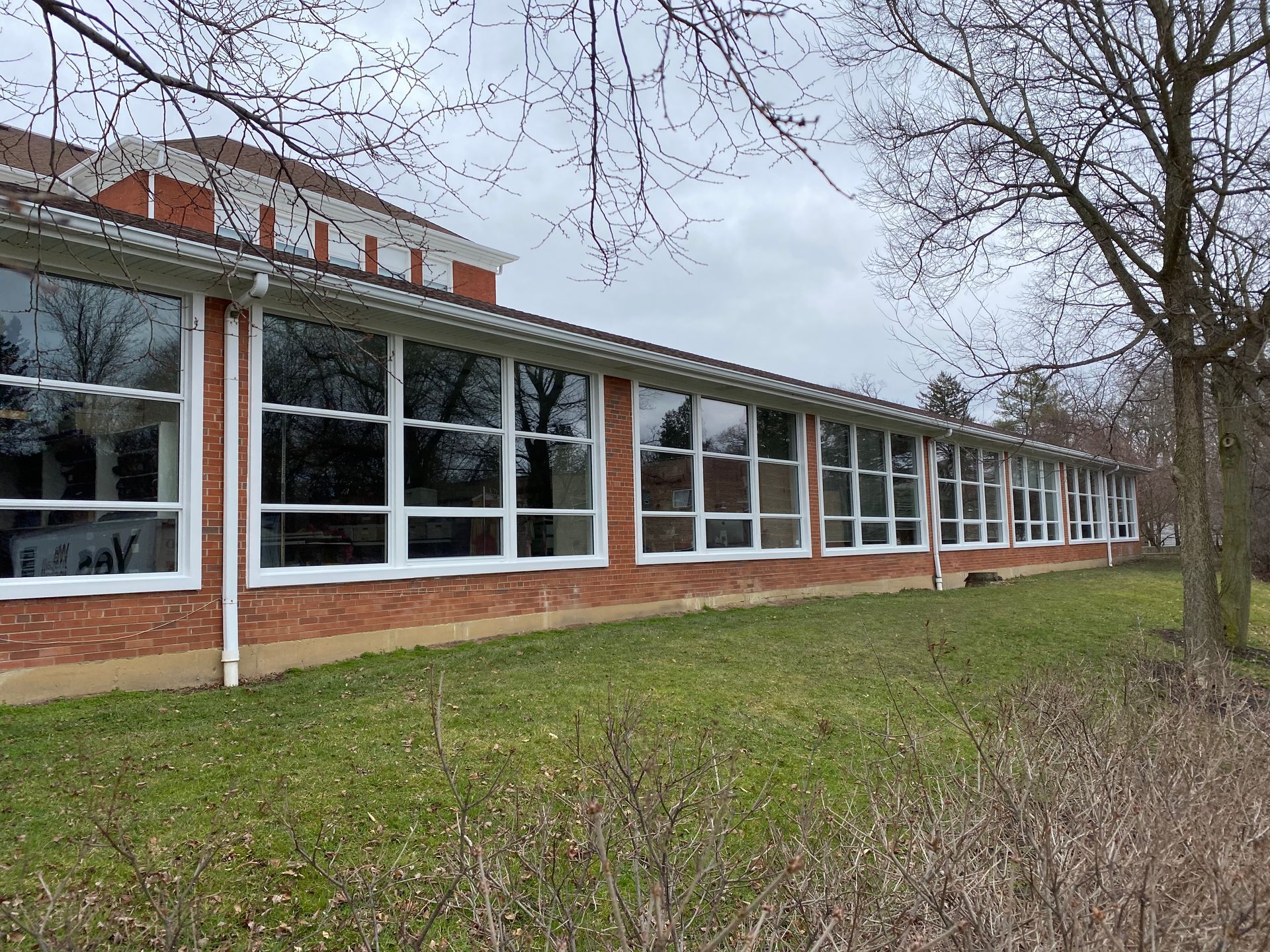 A large brick building with a lot of windows is surrounded by grass and trees.