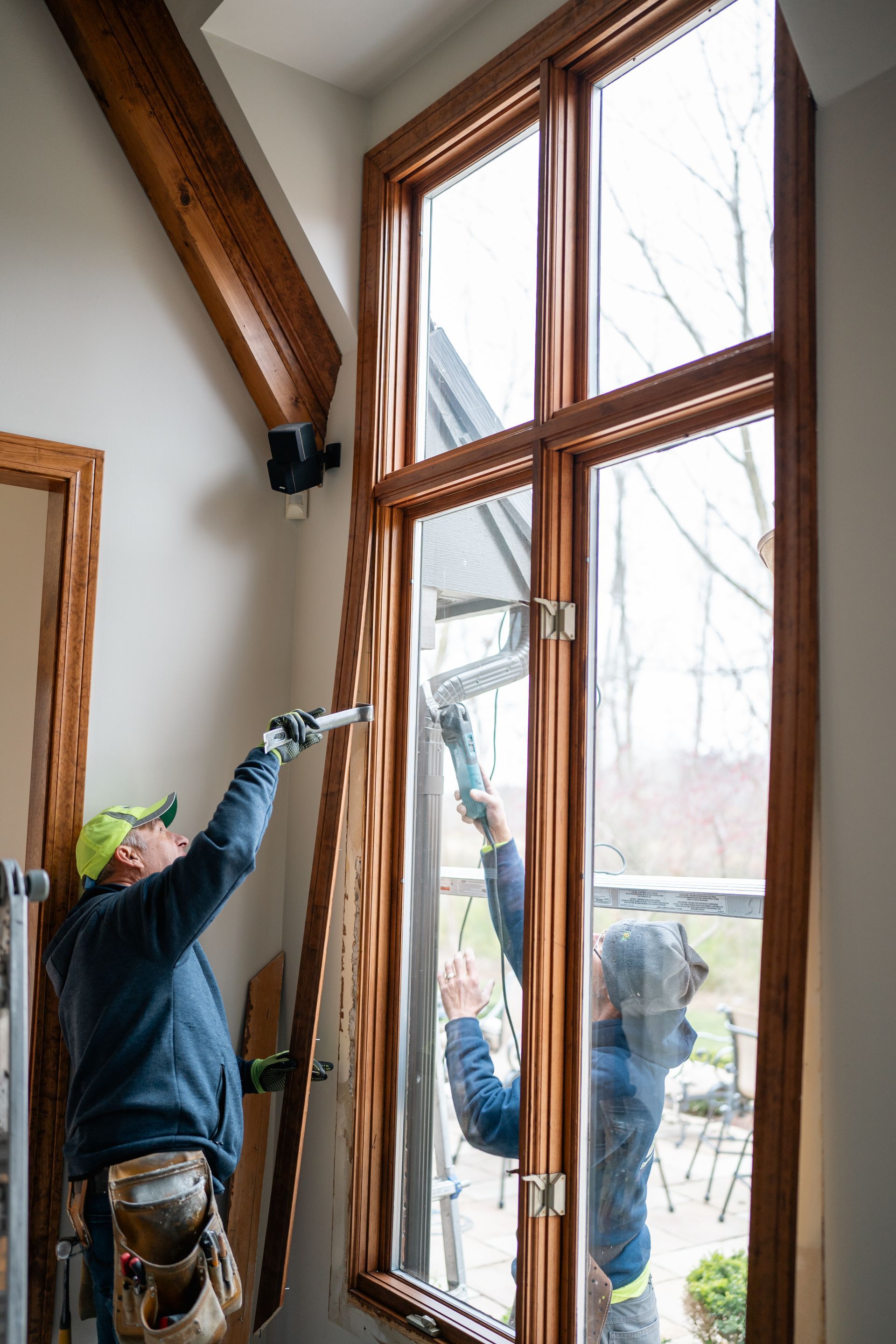 Two people installing a tall, multi-pane window in a light-filled interior. One holds a frame.