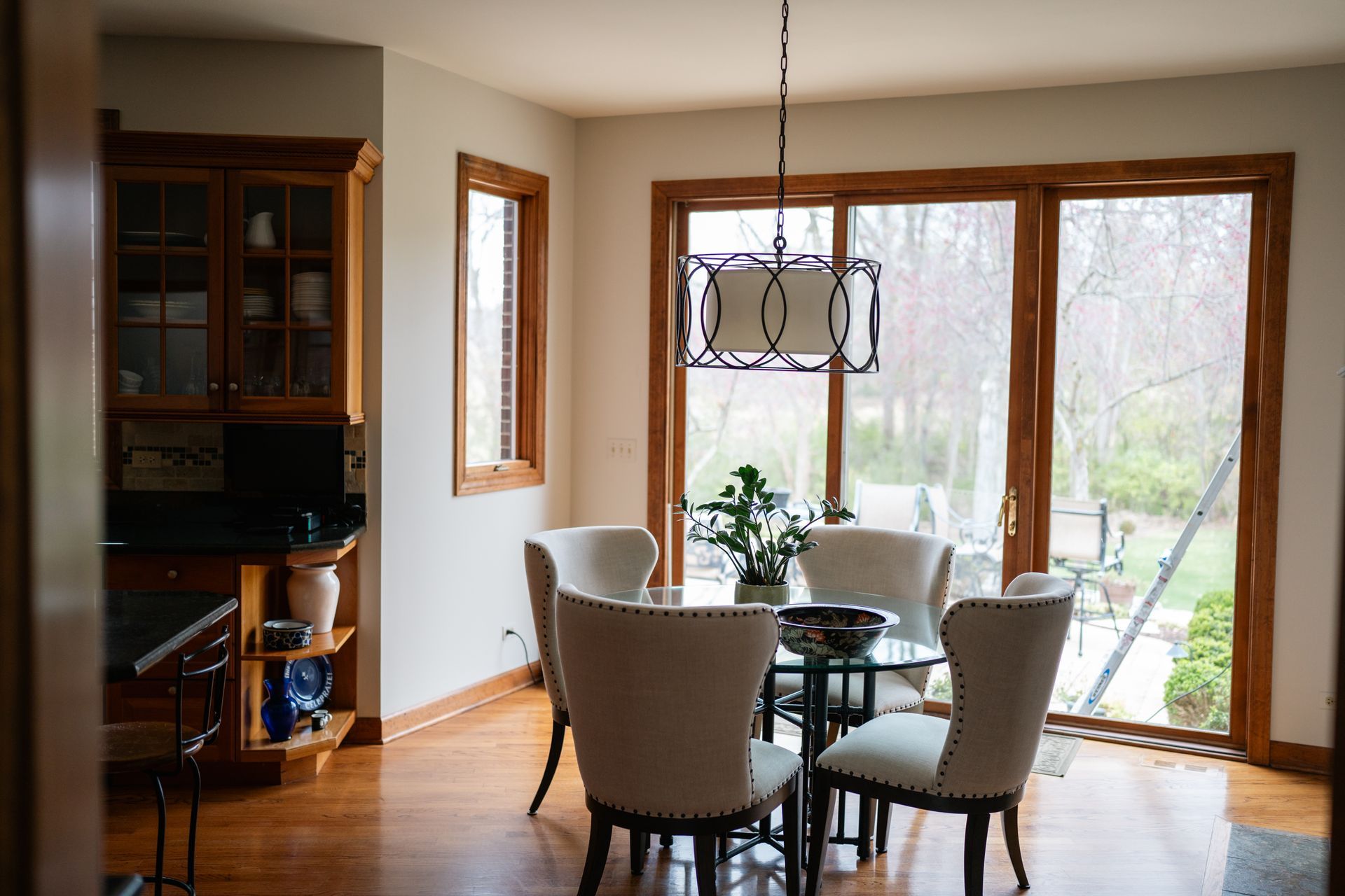 Dining room with round table, four chairs, and large windows overlooking a yard.