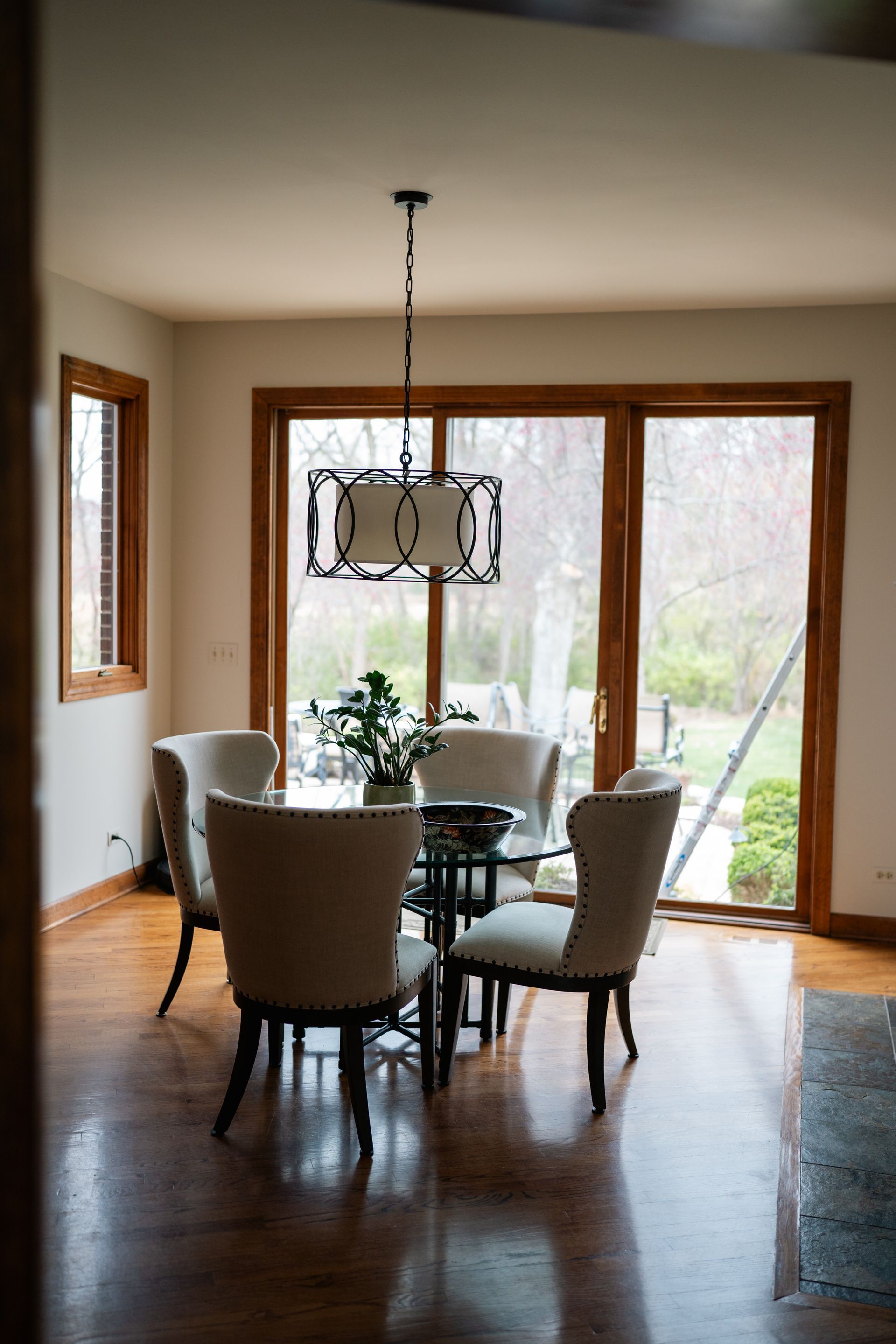 Dining room with glass table, four chairs, and a chandelier; large window.