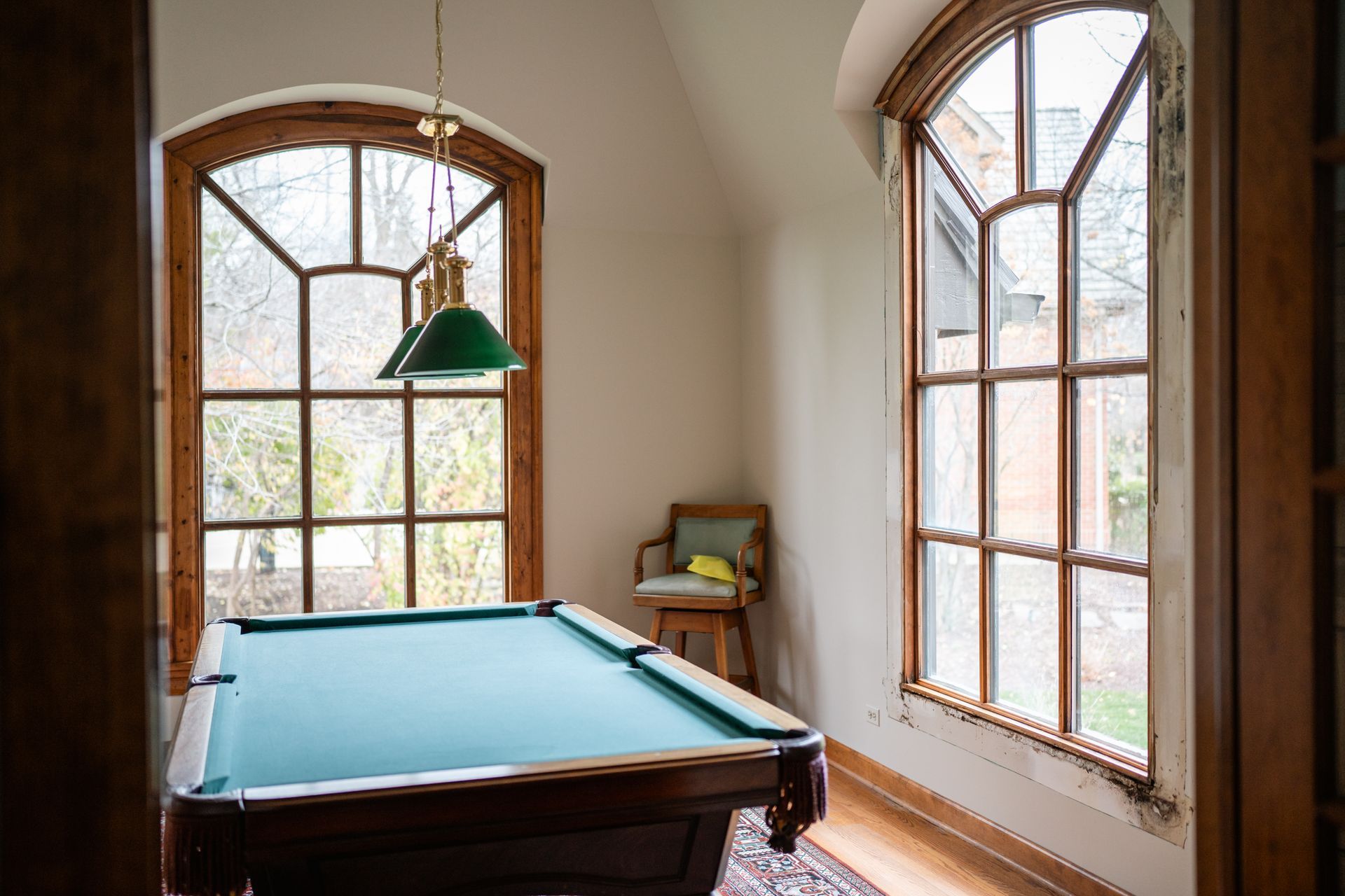 Pool table in a room with arched windows, green felt, and a hanging light fixture.