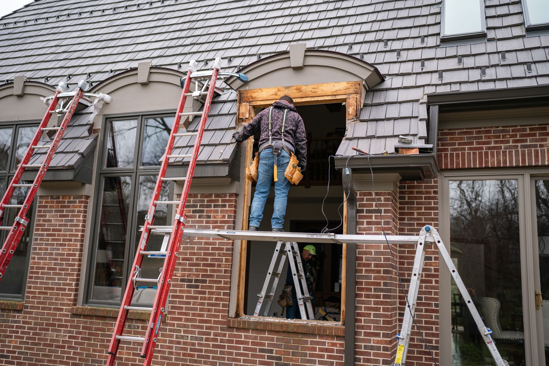 Man on scaffolding installing a window in a brick building. Ladders and tools are visible.
