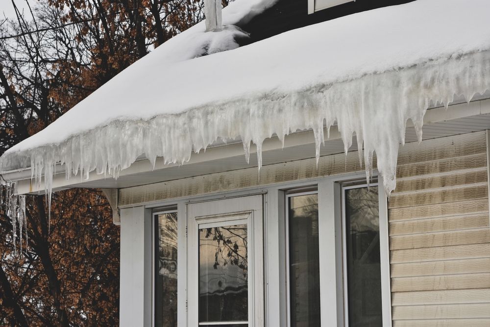 Icicles hanging from a snow-covered roof over windows.