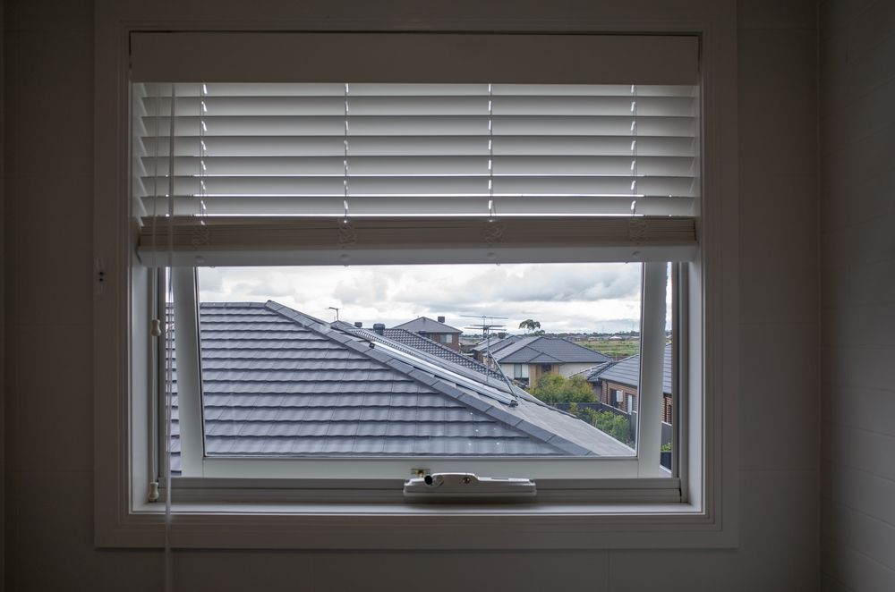 A window with blinds and a view of a roof.