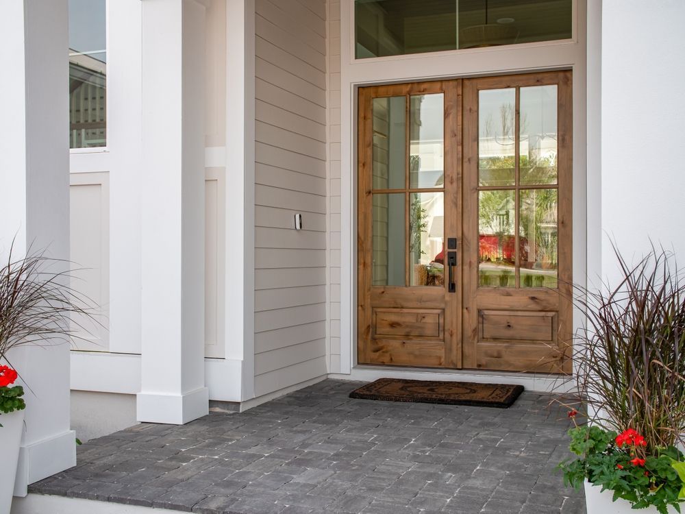 A front porch of a house with a wooden door and a door mat.