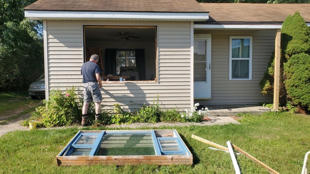 A man is standing in front of a house with a window open.