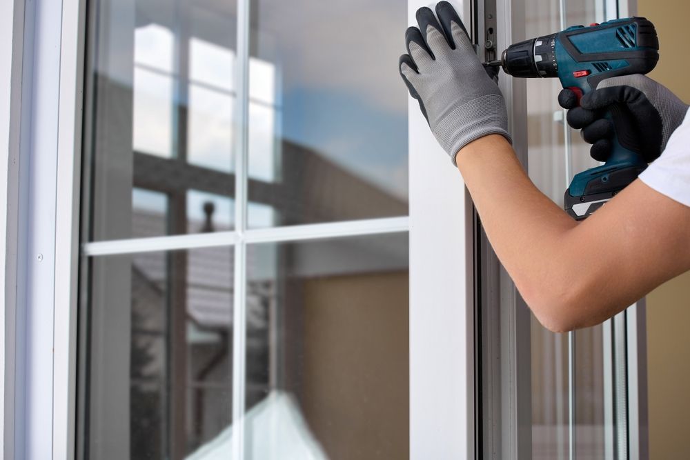 Person in gloves using a drill to install a white window.