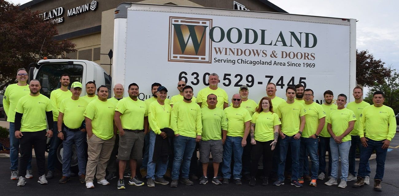 A group of people are posing for a picture in front of a woodland windows and doors truck.