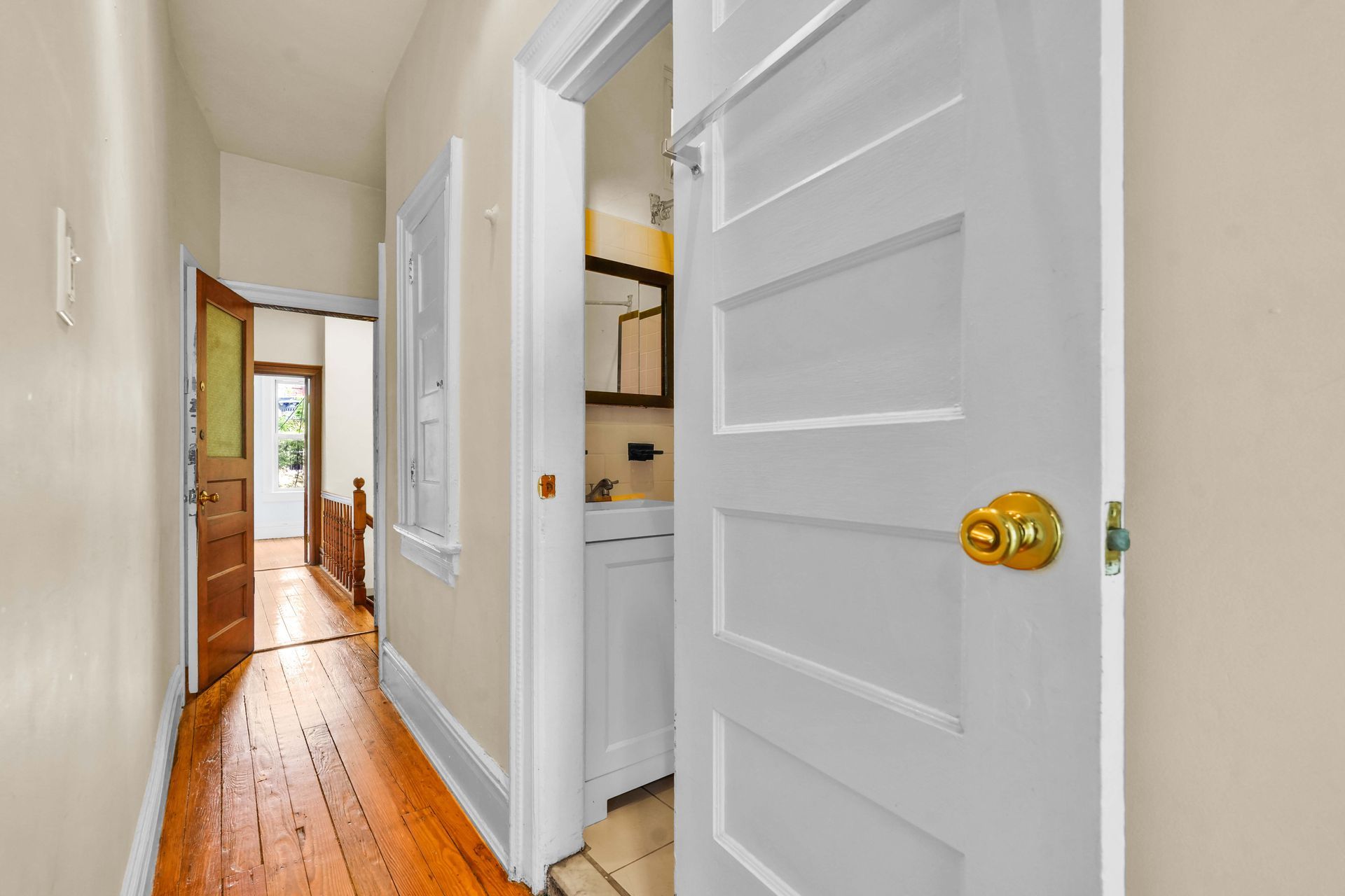 A hallway with wooden floors and white doors leading to a bathroom.