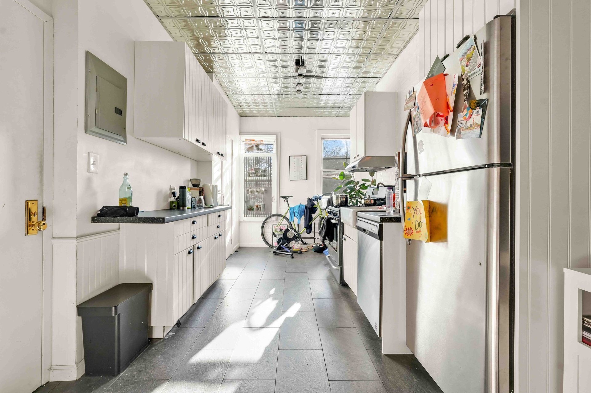 A long kitchen with white cabinets and a refrigerator.