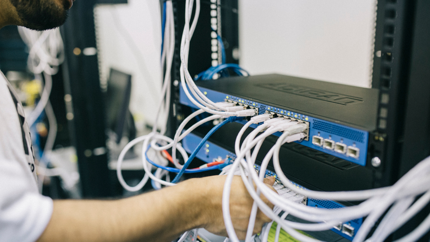 Blue network switch with tangled Ethernet cables in a server rack, with a person partially visible nearby