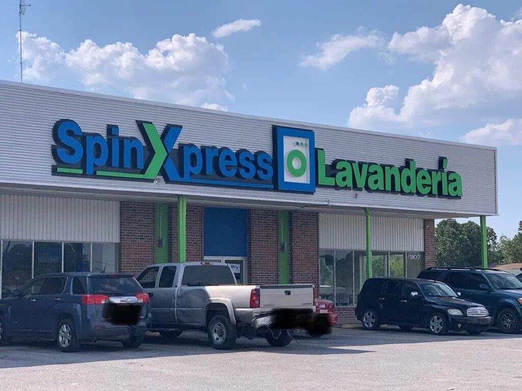 Spinxpress lavanderia storefront with parked cars under a partly cloudy sky