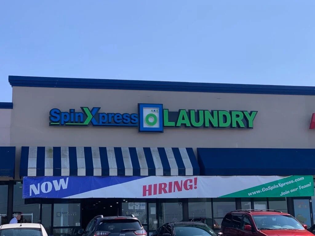 Spinxpress Laundry storefront with blue awning and a bright “NOW HIRING!” banner.