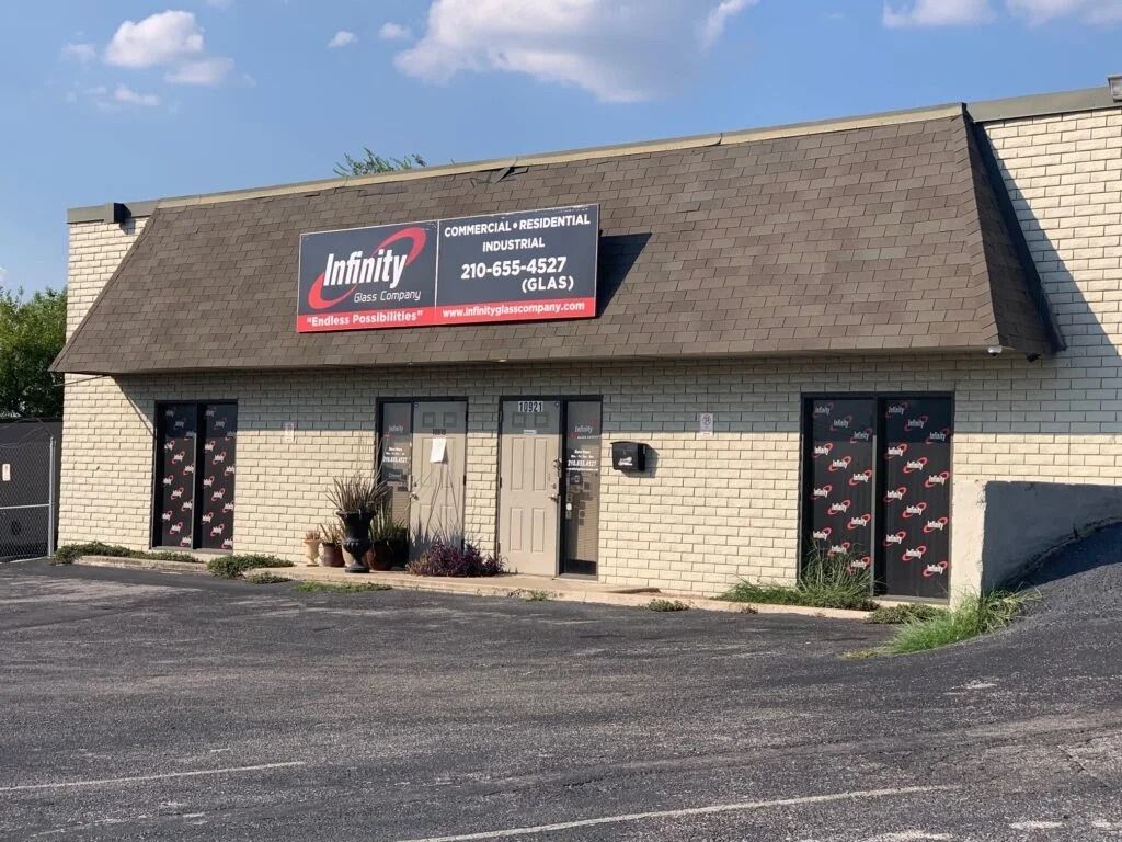 Small tan brick commercial building with a sign, dark doors, and a parking lot in front.