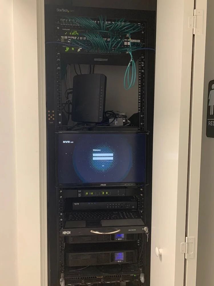 Open server rack with network equipment, patch cables, and a monitor in a closet.