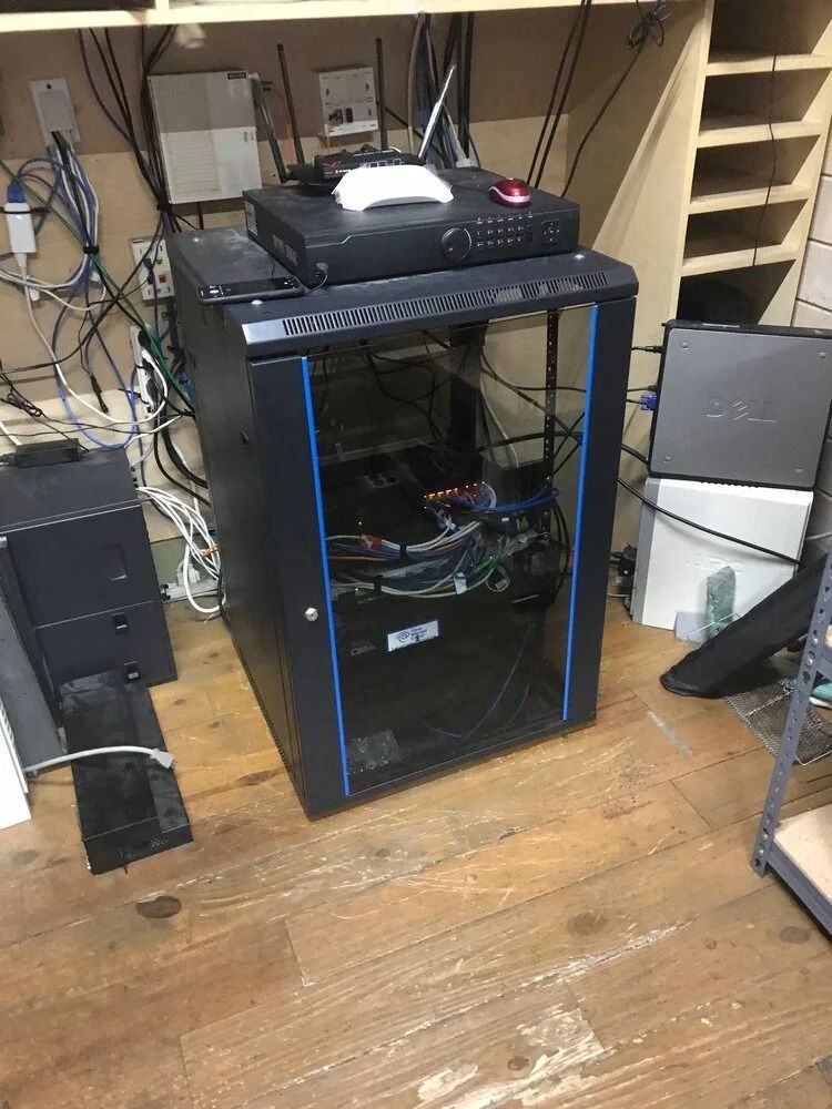 Black desktop PC tower with blue accents under a desk, surrounded by cables and equipment.