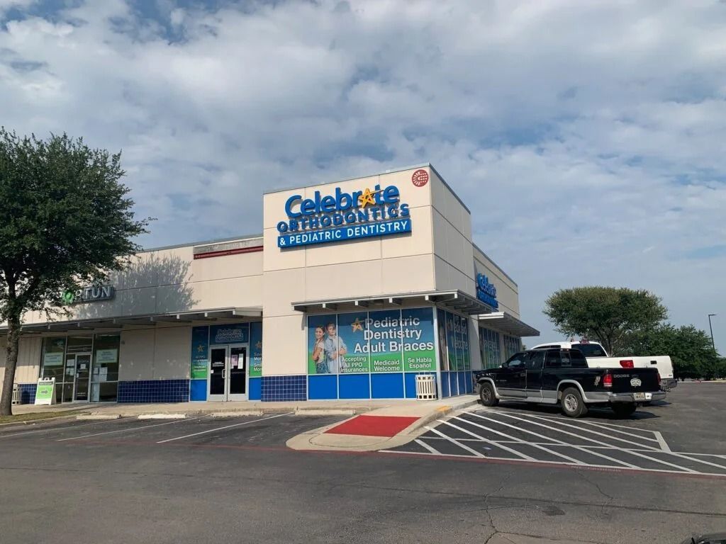 A Celebration Station storefront with blue trim, a black pickup truck, and a partly cloudy sky.