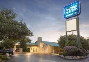 Two-story stone building at dusk with a bright blue hotel sign and parking lot in front