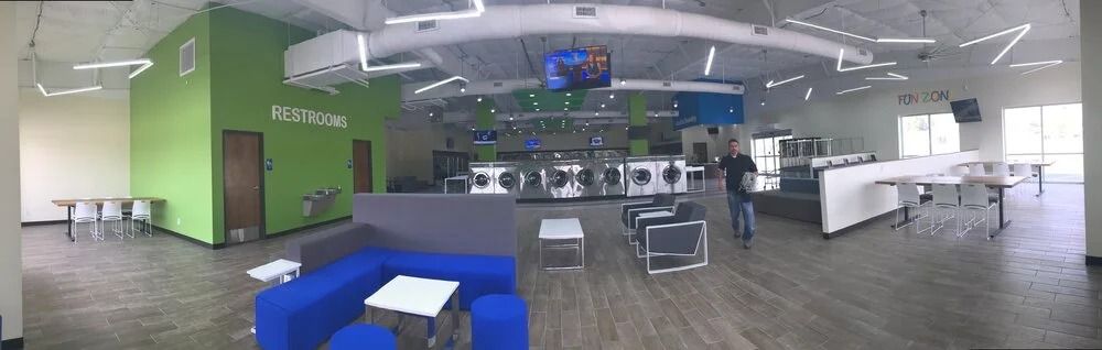 Modern office lounge with green and white walls, blue chairs, tables, and a large TV display