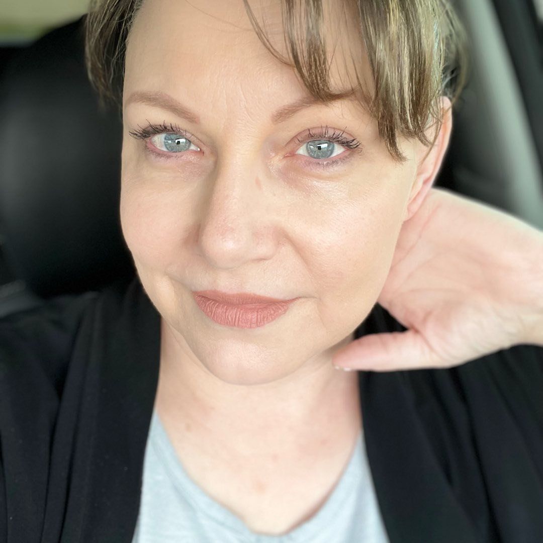A woman is sitting in a car with her hand on her neck.