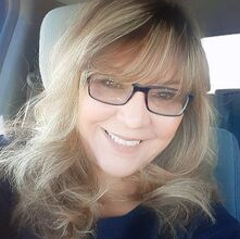 A woman wearing glasses is smiling while sitting in a car.