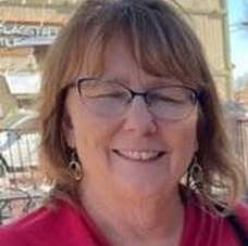 A woman wearing glasses and earrings is smiling for the camera.