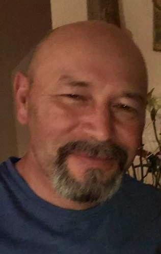 A bald man with a beard and mustache is wearing a blue shirt.