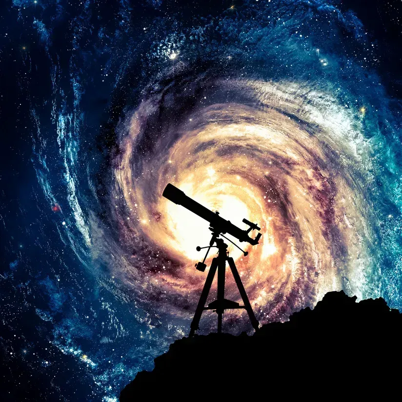Silhouette of a telescope on a hill against a glowing spiral galaxy sky