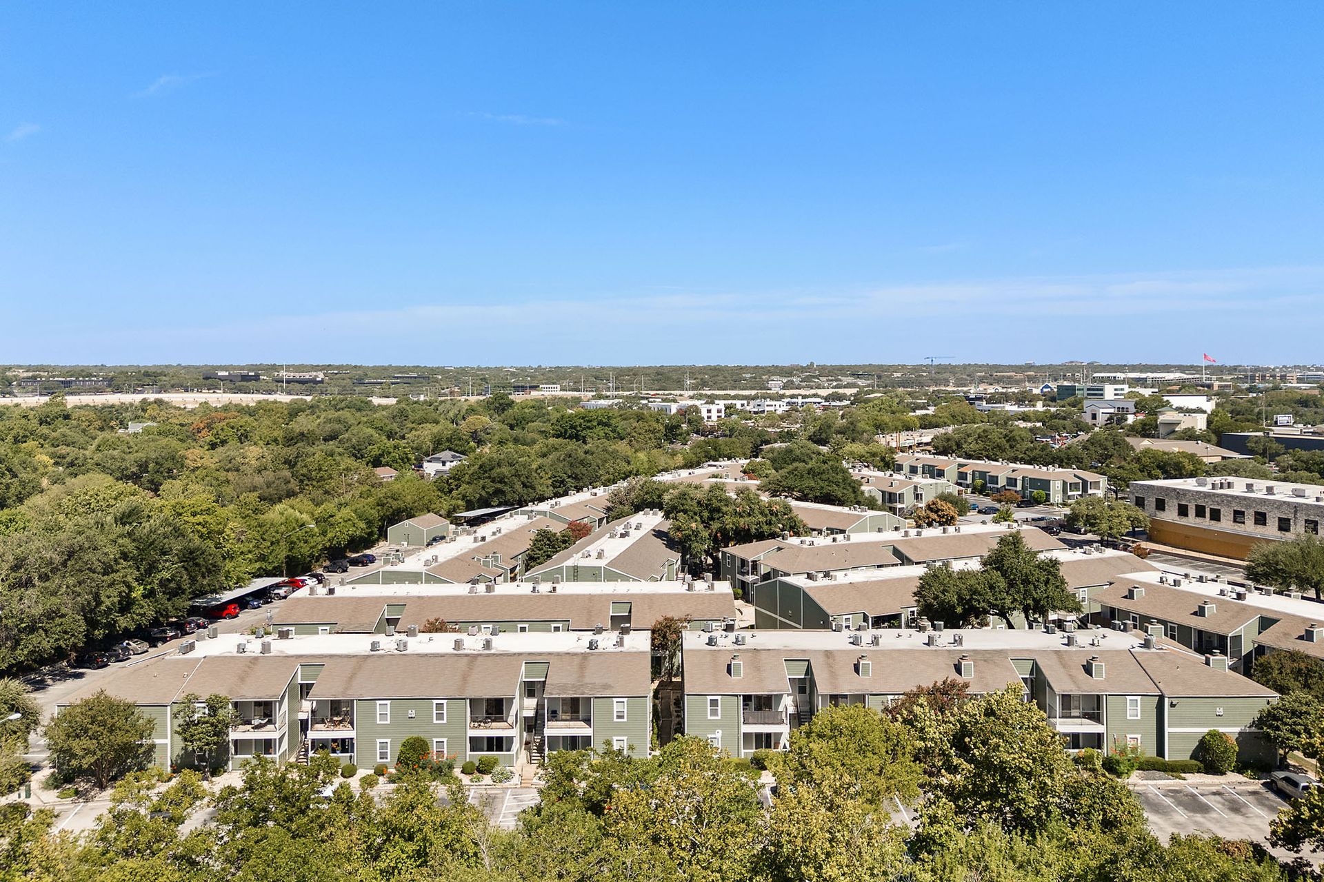 Aerial view of beige apartment buildings amid green trees under a clear blue sky