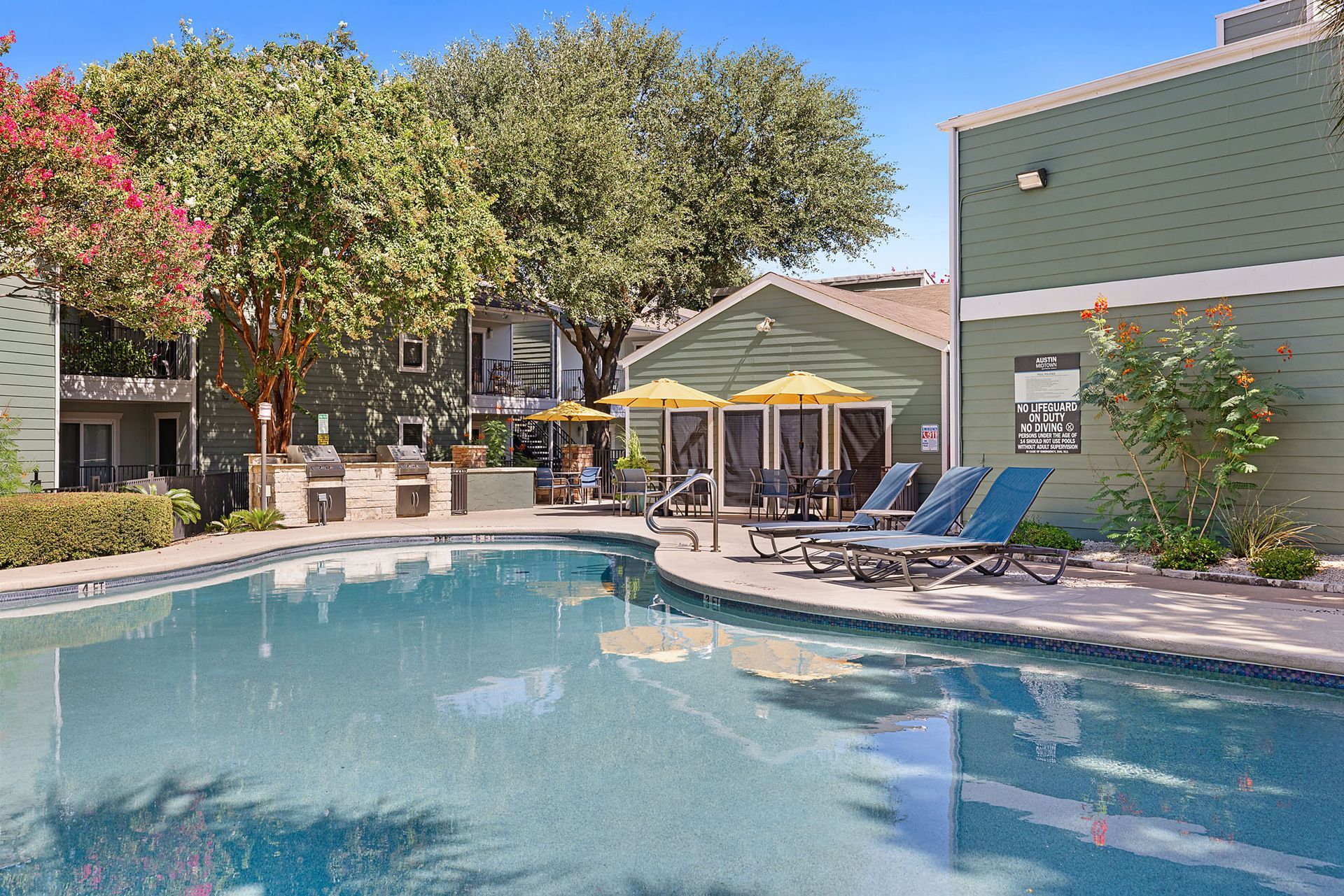 Apartment courtyard with a turquoise pool, lounge chairs, and lit buildings at dusk at Austin Midtown offers apartments in North Austin, TX.