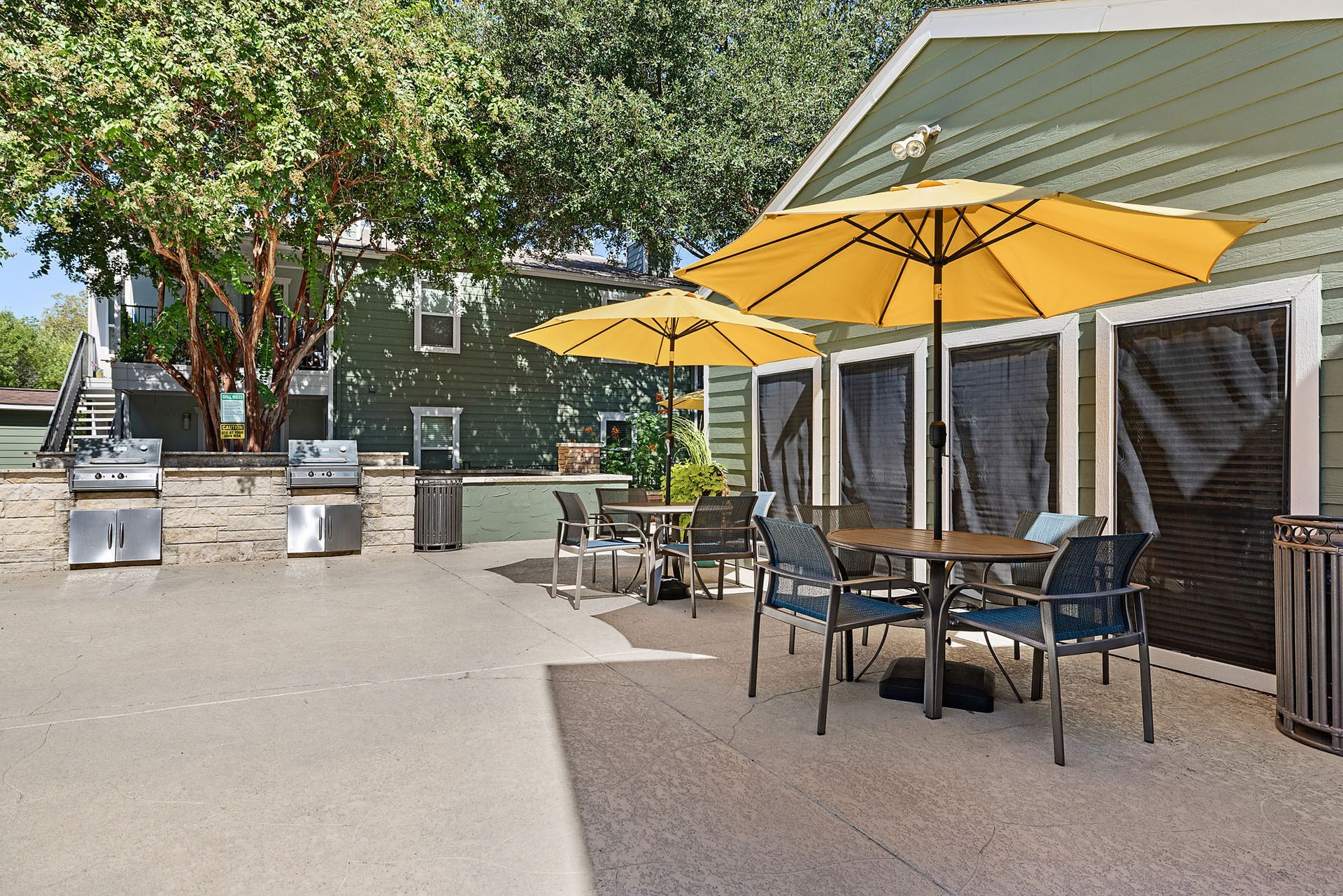 Outdoor café patio with yellow umbrellas, black tables and chairs, and trees in the background