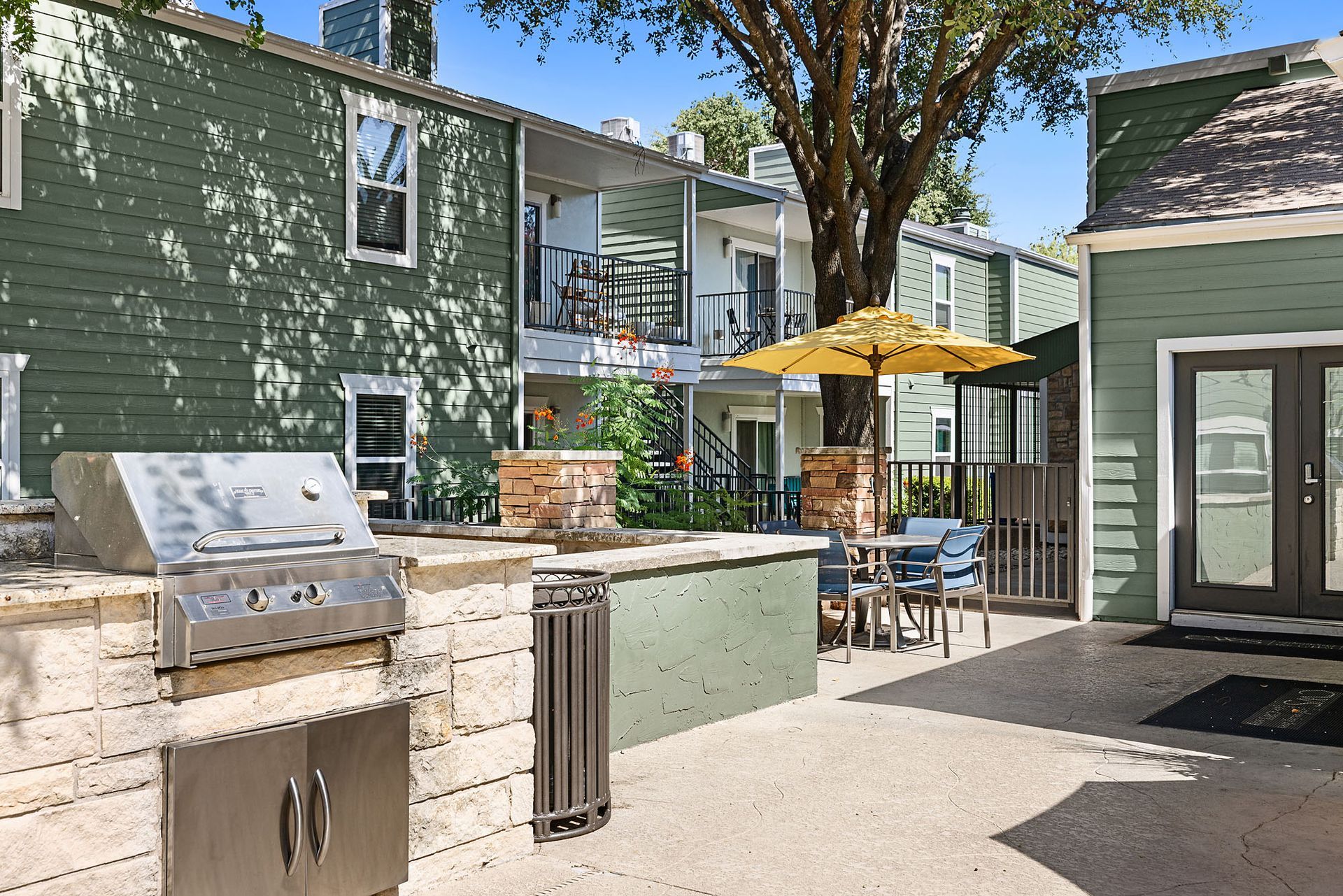 Outdoor patio with grill, tables, yellow umbrellas, and green buildings in the background