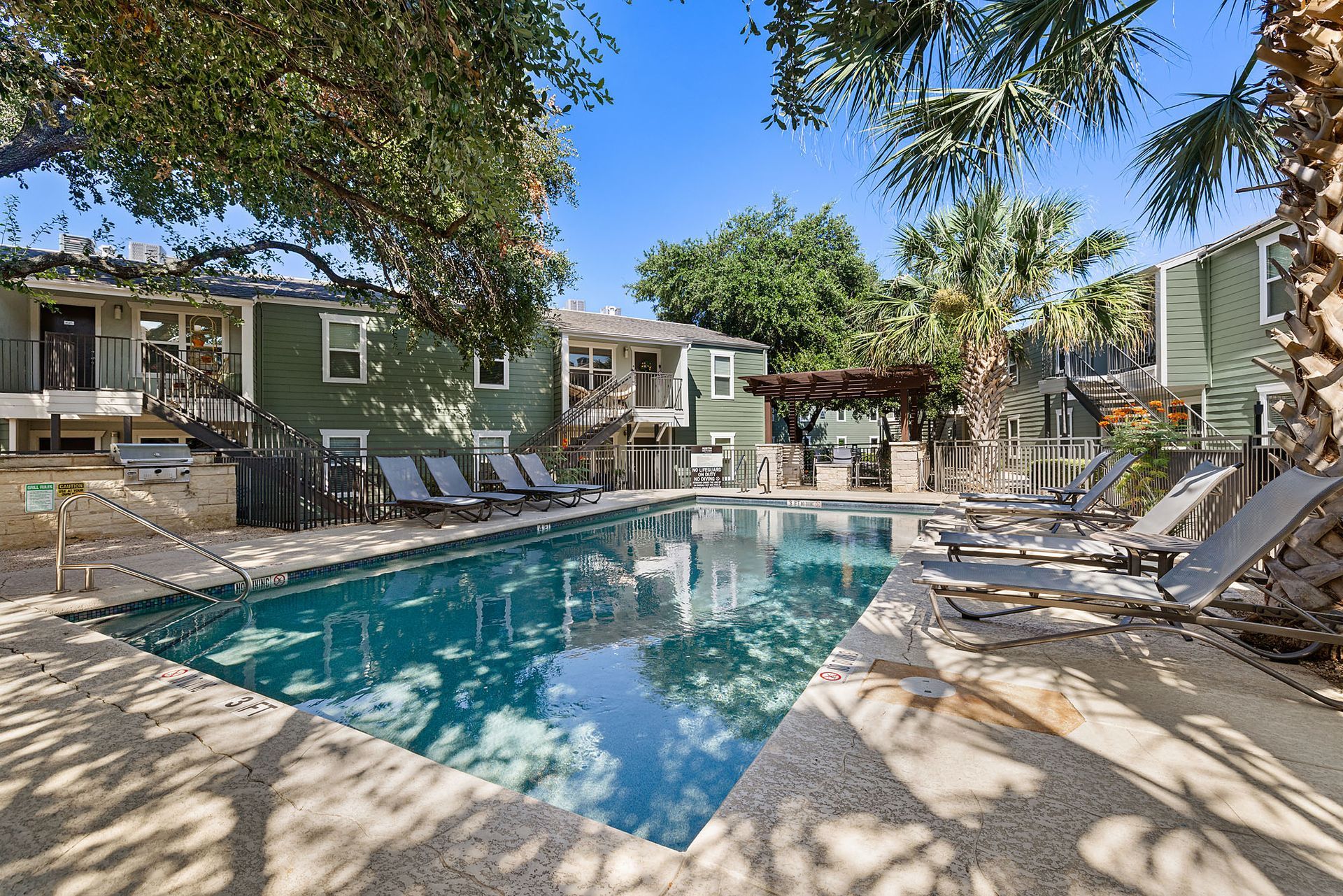 Apartment courtyard pool with lounge chairs and shaded trees around a turquoise swimming pool