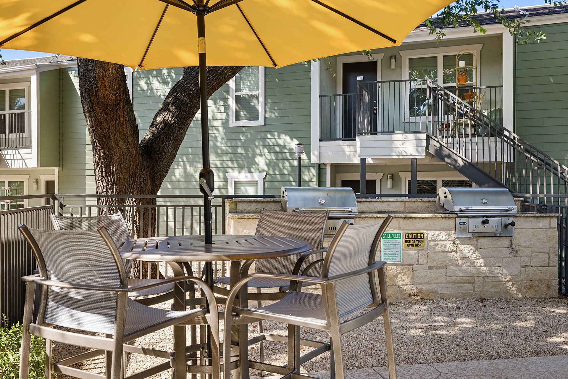 Outdoor patio with wicker chairs, glass table, and yellow umbrella in front of a house