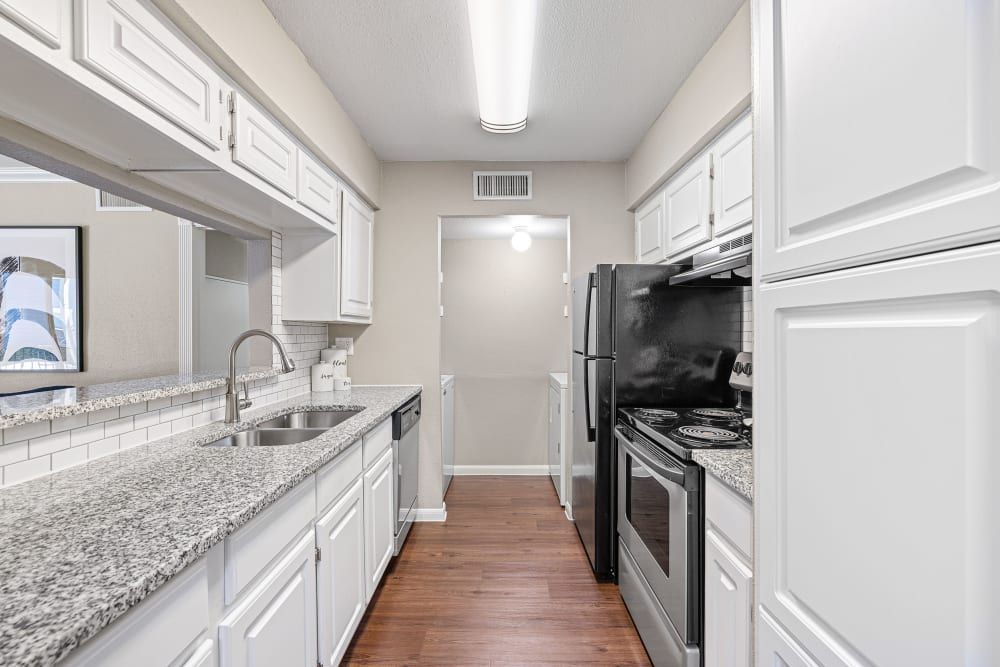Modern narrow kitchen with white cabinetry, granite countertops, stainless steel appliances, and dark wood flooring at Austin Midtown in North Austin, TX.