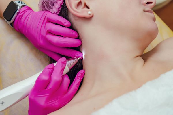 Gloved hands performing a neck injection on a person lying down, with a syringe and smartwatch visible