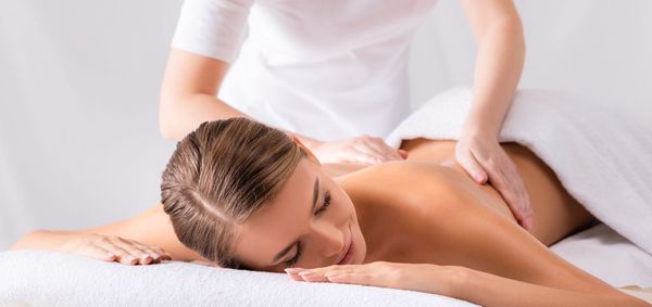 Massage therapist giving a back massage to a woman lying face down on a spa table
