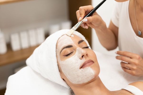 Facial spa treatment with a mask being brushed onto a reclining client