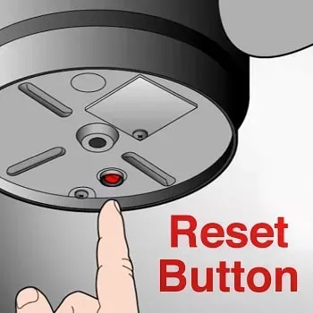 Hand pressing a red reset button on the bottom of a garbage disposal unit.