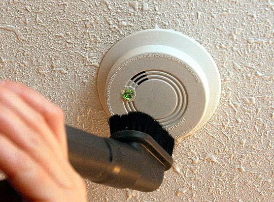 Person vacuuming a smoke detector on a textured wall.