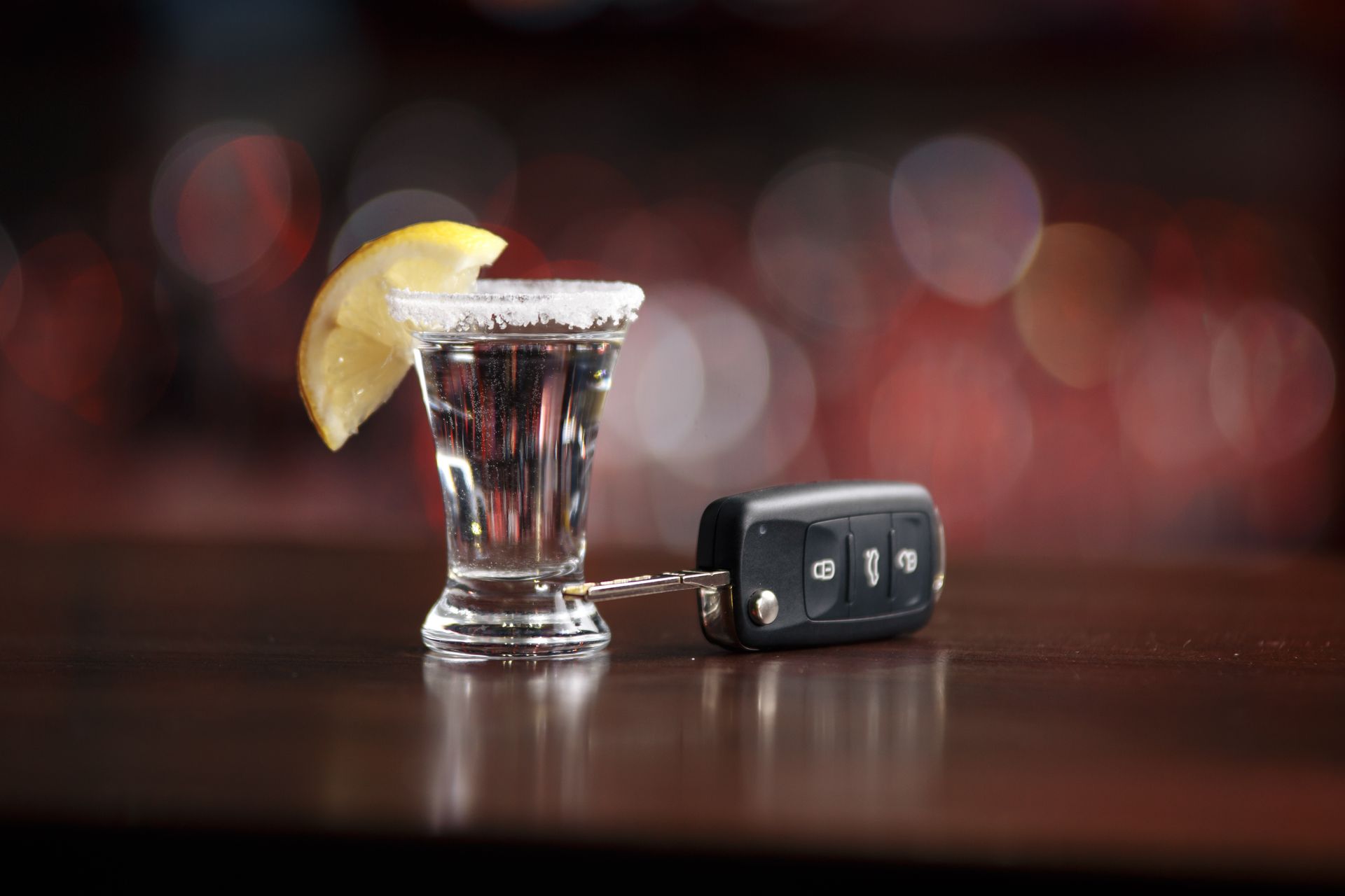 Shot glass of liquor with car keys on a bar; a warning against drunk driving.