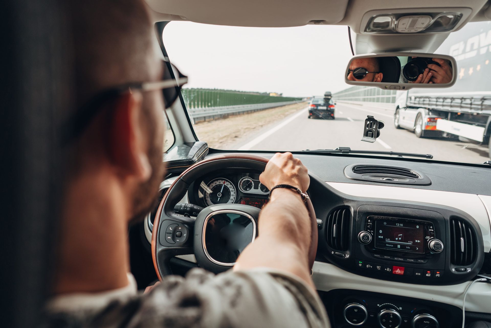 Driver’s view from inside a car on a highway, with a hand on the steering wheel and vehicles ahead