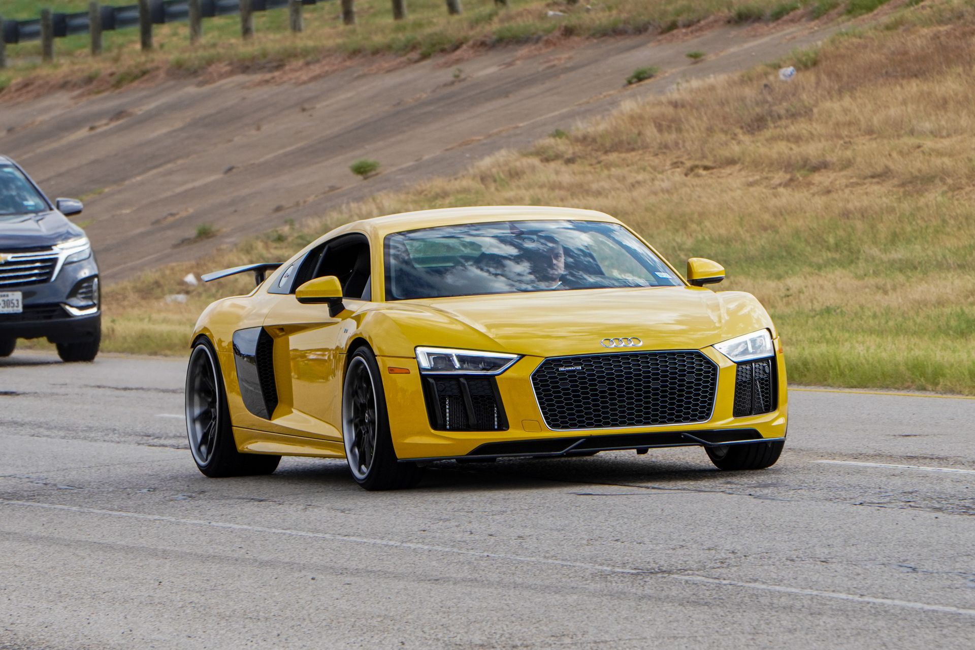 Yellow Audi R8 with twin turbos captured from a front 25-degree angle, surrounded by greenery at the edges of the photo, in front of a shop.