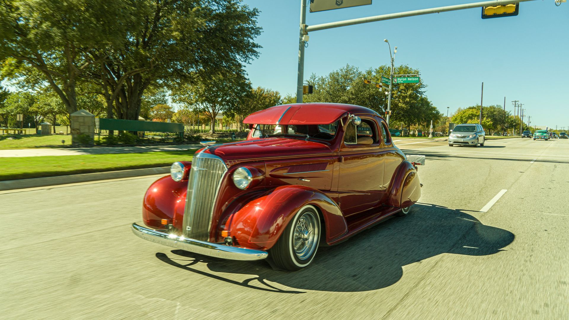 1937 Chevrolet Master Coupe in red captured in a rolling shot while driving down a main street in a town.