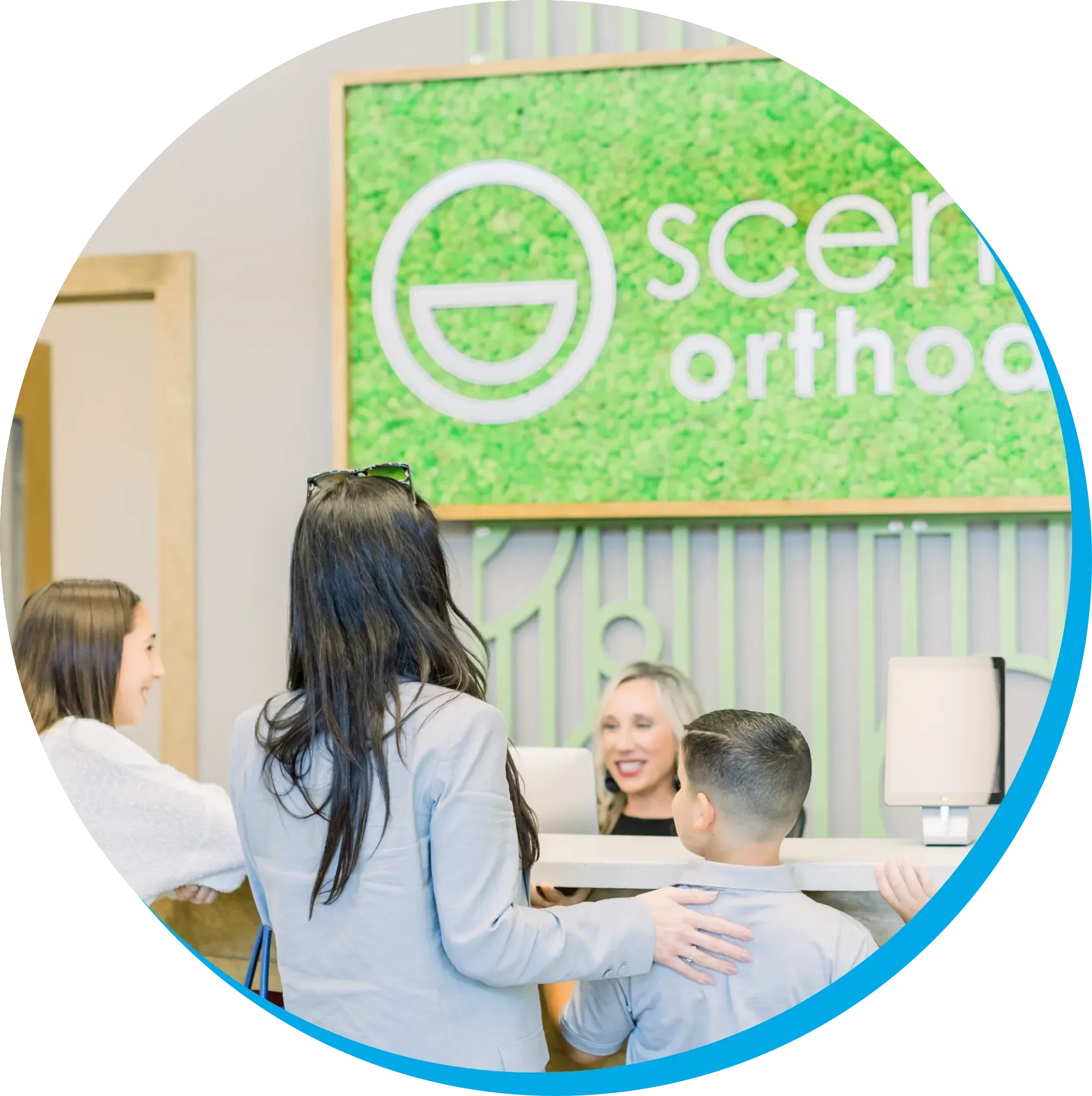 A group of people are standing in front of a scenic orthodontics reception desk.