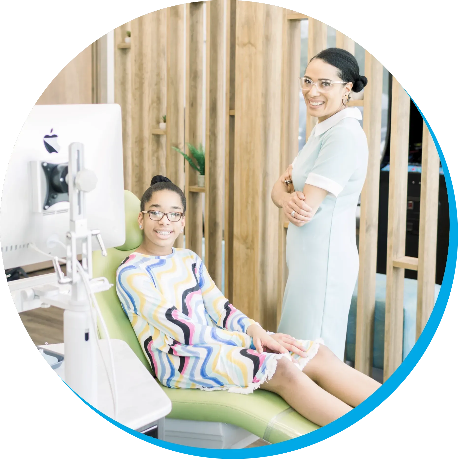 A woman is standing next to a girl in an orthodontic chair.